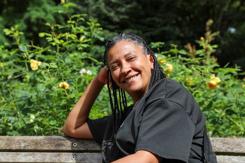 Kelly sitting on a bench, leaning her head on her arm and smiling at the camera