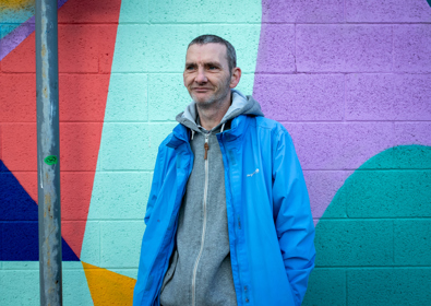 A man in a blue jacket standing in front of a colorful, geometric mural.
