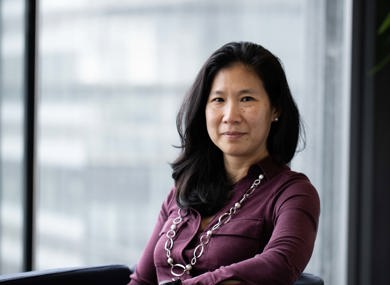 Portrait of a woman wearing a purple dress, sitting indoors with a window background that filters soft natural light.