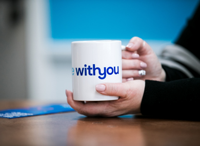 Close-up of a person's hands holding a white mug with the words "Withyou" in blue text.