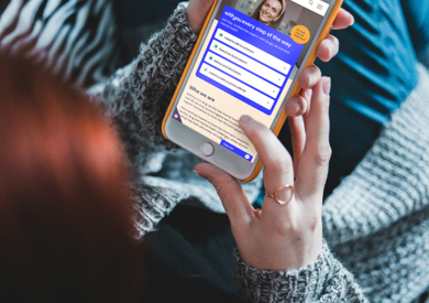 Person in gray sweater holding a phone displaying the WithYou support website, sitting on a zebra-patterned blanket.