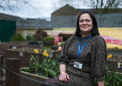 A woman in a leopard print dress, wearing a lanyard around her neck, sitting on a wooden ledge in a garden with blooming daffodils.