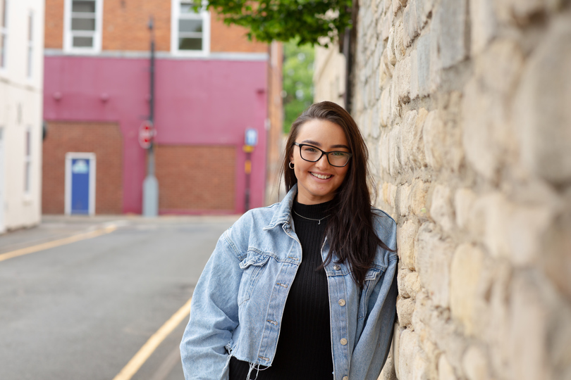 Beth, leaning against a wall, smiling at the camera