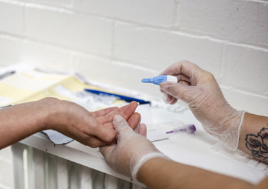 Healthcare worker in gloves performing a blood test on a patient's finger in a clinical setting, with medical supplies around.