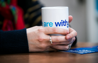 Close-up of a person's hands holding a white mug with the words "Withyou" in blue text.