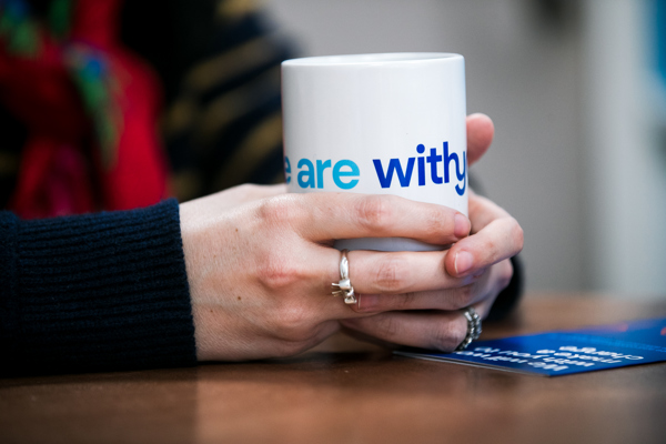 Close-up of a person's hands holding a white mug with the words "Withyou" in blue text.